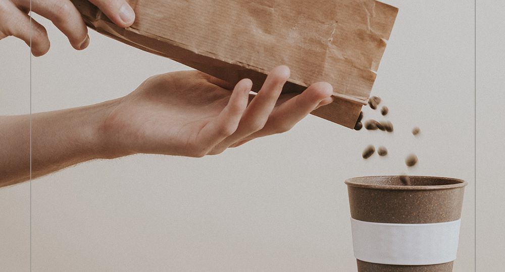 Hand pouring coffee beans from a paper bag into a coffee cup